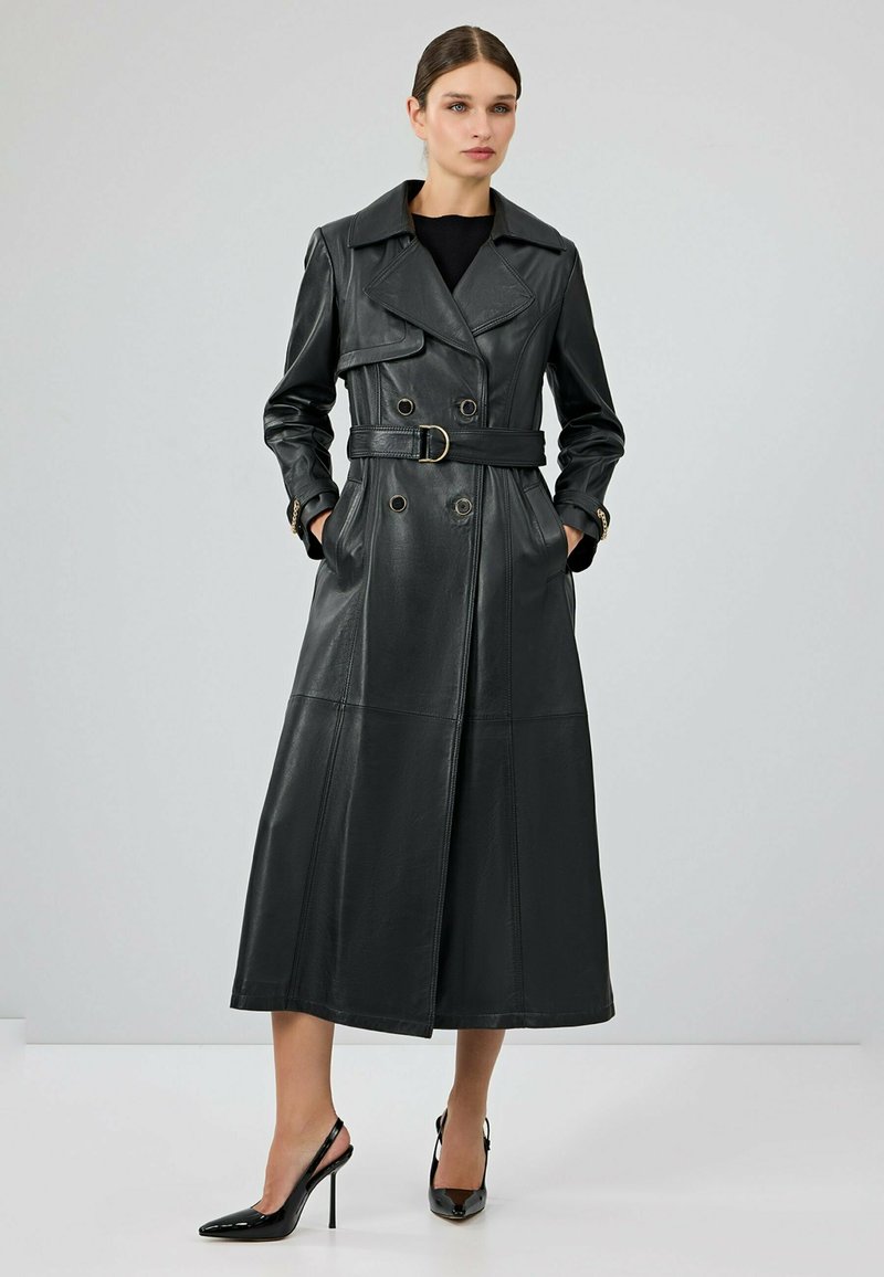 Zwarte leren trenchcoat met een dubbelgeknoopte ontwerp, brede kraag, een tailleriem en lange mouwen. Voorzien van zijzakken en een vloeiende silhouet.