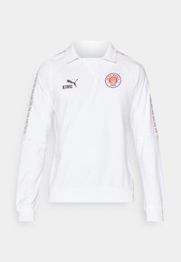 Witte lange mouwen jersey met een polo kraag, bruin logo en tekst, gedessineerde accenten op de mouwen en ribgebreide manchetten.