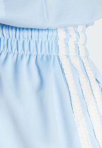 Ljusblå shorts med elastisk midja, med vit volang längs sidorna och en mjuk, slät textur.