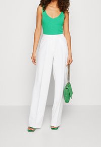 Canotta verde a coste, pantaloni bianchi a vita alta con gamba larga, sandali verdi con cinturini e borsa verde testurizzata con manico a catena.