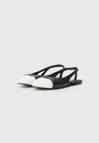 Zapatos planos en blanco y negro con punta afilada, con parte superior negra y punta en cuero blanco, lados abiertos y una delicada correa en el tobillo.