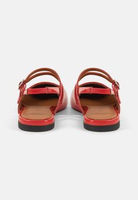 Red patent leather sandals with open backs, two narrow straps across the ankle, and a flat black rubber sole. Smooth finishes and minimal detailing.