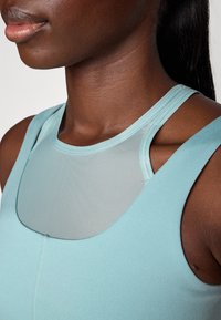 Light blue athletic top with a smooth texture, featuring a mesh panel at the neckline and fitted design. Stitched details accentuate the shape.