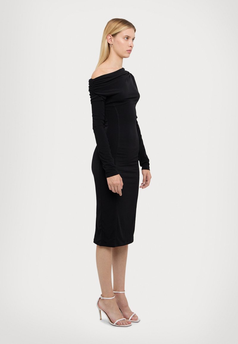 Rochie neagră cu umeri descoperiți, cu mâneci lungi, design mulat, detalii pliate la decolteu și tiv până la genunchi. Purtați cu sandale cu bretele.