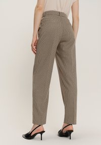Pantaloni alti a quadri marroni con gamba dritta, dotati di tasche laterali e passanti per cintura. Abbinati a scarpe slingback nere.