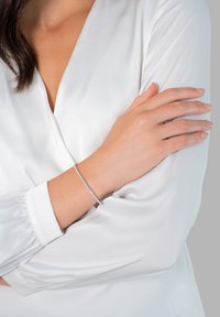 Sidabrinė apyrankė su subtilia grandinėle, puošiasi mažomis blizgančiomis detalėmis. Nešiojama ant riešo, derinama su balta ilga rankovėmis palaidine.