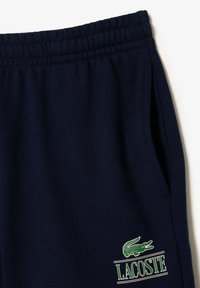 Pantalones deportivos color navy fabricados con un tejido suave, que cuentan con una cintura elástica, bolsillos laterales y un detalle del logo bordado en verde de Lacoste.