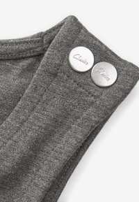 Grauem Stoff mit glatter Textur und zwei silbernen Knöpfen, die mit "Clarks" beschriftet sind. Die Knöpfe haben eine polierte Oberfläche mit leichtem Glanz.