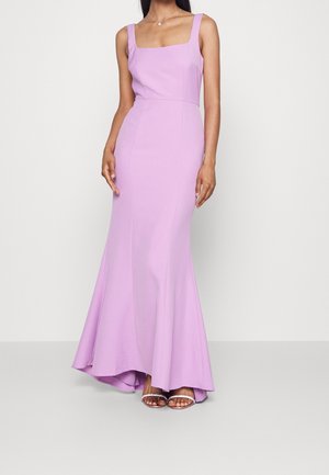 Femme portant une robe de soirée lilas ajustée sans manches avec un décolleté carré et un ourlet évasé, associée à des talons ouverts argentés.