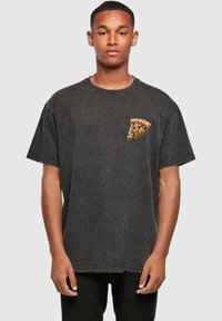 Camiseta negra de gran tamaño hecha de algodón con un acabado desgastado. Presenta un gráfico colorido de una porción de pizza en la zona izquierda del pecho.