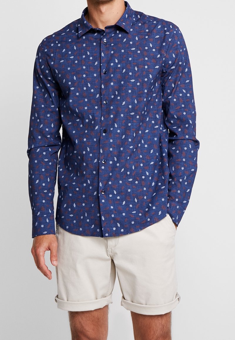Koszula z długim rękawem w granatowym kolorze z liściastym wzorem w czerwono-białe. Wykonana z teksturowanej tkaniny, z guzikiem z przodu i kołnierzykiem.