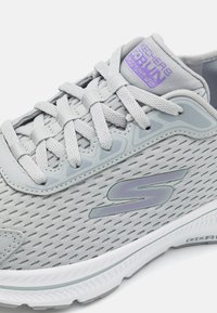 Gray athletic shoe featuring breathable mesh upper, textured accents, and reflective logo. Lace-up design with a cushioned sole.