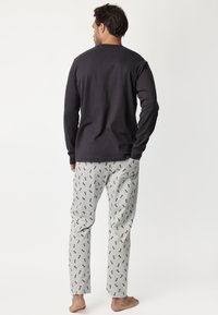 Camisa de manga larga gris oscuro combinada con pantalones de pijama gris claro que presentan un patrón repetido de pequeños iconos en rojo y negro.