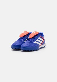 Blå atletiska fotbollsskor med en texturerad syntetisk ovandel, vita ränder och klara orange detaljer på tungan och hälen.
