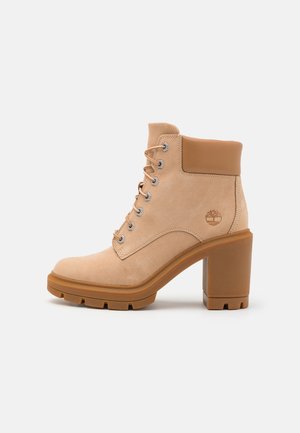 Beiger Wildleder-Stiefelette mit gepolstertem Kragen, Schnürverschluss vorne, massivem Blockabsatz, profilierter Sohle und Timberland-Baum-Logo an der Seite.