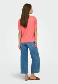 Koraalroze top met korte mouwen en een gestructureerd patroon, gecombineerd met losse blauwe denim jeans en bruine slidesandalen. Eenvoudig, casual ontwerp.