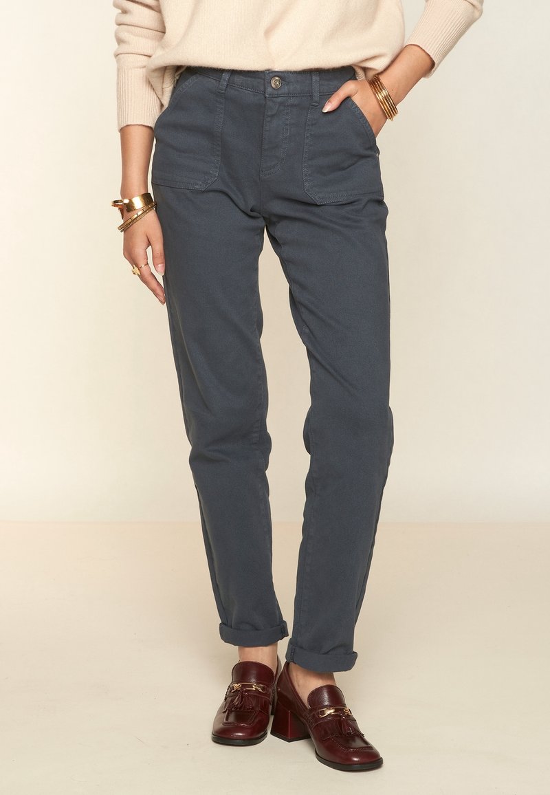 Pantalones de un gris pizarra ajustados con cintura alta, bolsillos frontales y puños enrollados, combinados con mocasines de tacón burdeos.