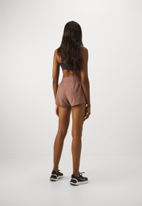 Top deportivo gris oscuro y pantalones cortos deportivos lila claro con cintura fruncida, que presentan una textura suave y un diseño minimalista. Zapatillas negras.