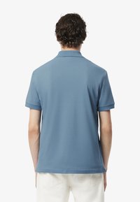 Niebieska koszulka polo z krótkim rękawem i klasycznym kołnierzykiem. Gładki materiał, proste linie i minimalne detale przeszycia. Stylizowana z białymi spodniami.