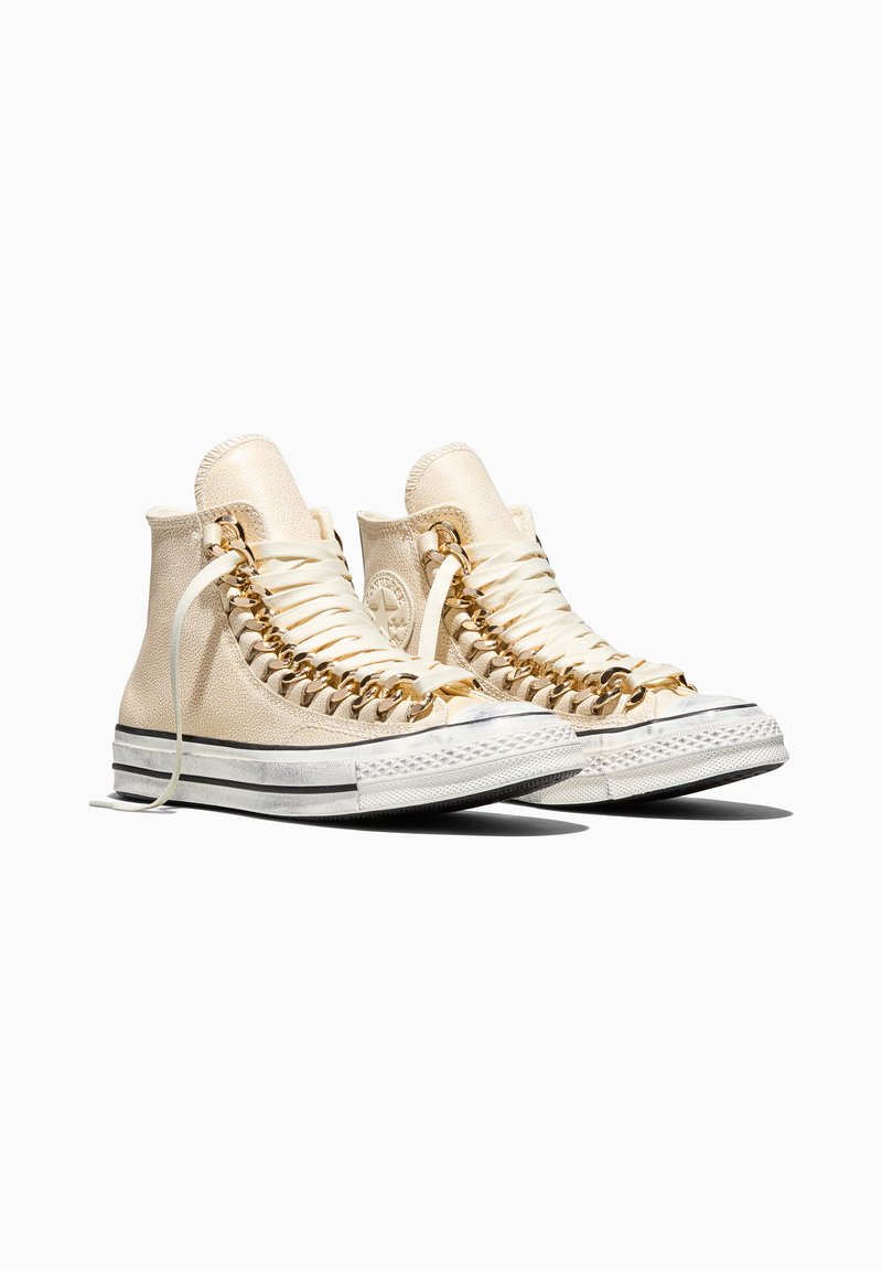 High-top beige sneakers with white soles and golden chain laces, shown side by side on a white background.