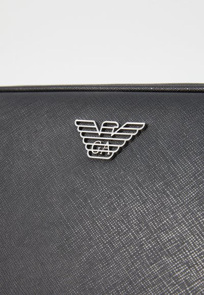Black textured material, featuring a metallic silver emblem with layered wings and "GA" detail at the center, attached to the surface.