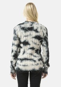 Knit sweater with a black and white tie-dye pattern. Features ribbed cuffs and hem, textured cable knit design, and frayed edges.