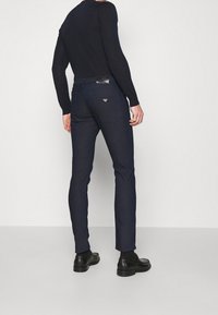 Mörkblå slim-fit jeans med en läderlogga på baksidan av midjan, med två bakfickor och en slät textur.