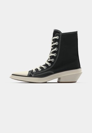 Czarne wysokie buty z płótna z białymi sznurówkami, kremowa osłona palców i charakterystyczny kanciasty kremowy obcas. Białe przeszycia.