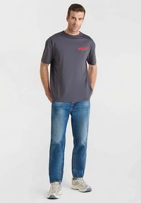 Grijs T-shirt met rode print, korte mouwen, gecombineerd met lichtblauwe jeans met rechte pijpen en grijze sneakers. Simpel, casual ontwerp, zonder patronen.