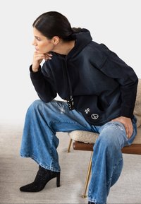 Black hooded sweatshirt with embellishments, paired with distressed blue wide-leg jeans and black heeled ankle boots. Textured fabric.