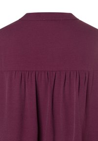 Bordeauxfarbene Bluse mit einem Kragen, die ein gefaltetes Rückendesign und eine glatte Textur aufweist. Normale Passform ohne sichtbare Verzierungen.