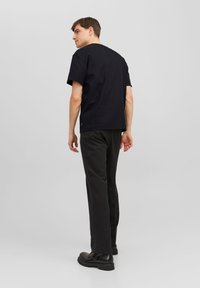 Camiseta de algodón negra con un corte relajado, mangas cortas y un escote redondeado, combinada con pantalones negros y calzado negro resistente.