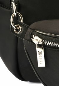 Czarna torba nylonowa z srebrnymi akcentami, z zamkiem błyskawicznym i wyraźną etykietą z logo. Gładka faktura i elegancki design.