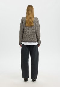 Maglione grigio a spina di pesce con maniche lunghe, abbinato a jeans denim neri larghi e décolleté nere a punta. Camicia bianca sotto il maglione.