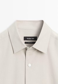 Chemise beige pour homme à boutons, avec col classique, premier bouton visible et étiquette "Massimo Dutti" à l'intérieur de l'encolure.