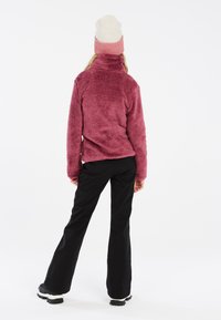 Fleece-pullover i vinröd, med hög krage, texturerat tyg och figurnära design. Matchas med svarta, vida byxor och svarta skor.