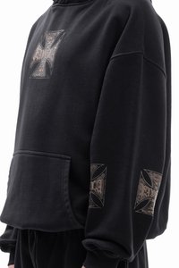 Black hoodie made of cotton, featuring a front pocket and large graphics on the sleeves. The design includes intricate silver patterns.
