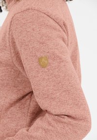 Sweatshirt i ett mjukt, dämpat rosa tyg med ett strukturerat mönster. Har en gummilagerad sköldlogotyp på vänster ärm.
