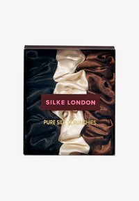 Set di quattro scrunchies in pura seta, nei colori nero, crema e due tonalità di marrone, presentati in una scatola quadrata trasparente con un'etichetta scura.