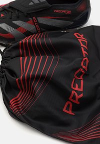 Zwarte voetbalschoenen met rode en grijze accenten, gecombineerd met een zwarte trekkoordtas met rode diagonale strepen en "PREDATOR"-tekst.