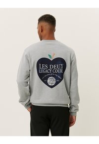 Γκρι φούτερ με στρογγυλή εκτύπωση που περιλαμβάνει σχέδιο μήλου, λογότυπο και τη φράση "για την αγάπη του Μεγάλου Μήλου," καθώς και ριπές μανικιών.