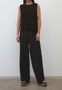 Top senza maniche a coste scure abbinato a pantaloni neri a gamba larga e scarpe scure con suola spessa. Design minimalista con texture morbide.