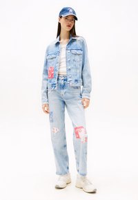 Svetlomodrá džínsová bunda s nášivkami, skombinovaná so svetlomodrými džínsami s ošúchanými miestami a červenými akcentmi. Biele tričko a tenisky dotvárajú celý look.