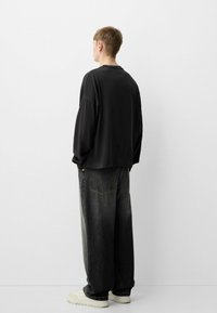 Musta ylisuurikokoinen collegepaita, jossa on tiputettu olkaimet, yhdistettynä tummiin farkkuihin, joissa on leveät lahkeet, sekä vaaleisiin lenkkareihin. Minimalistinen muotoilu, jossa on hienovaraisia metalliosia.