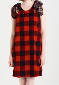 Rot-schwarz karierter ärmelloser Kleid mit gerüschten Karo-Trägern, das eine lockere Passform bietet und einen Saum knapp über dem Knie hat.