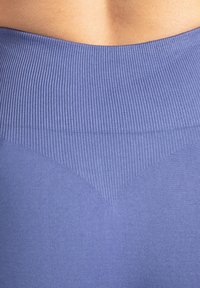 Leggings violettes sans couture avec une ceinture côtelée et un motif triangulaire à l'arrière. Texture douce, coupe ajustée et tissu extensible.