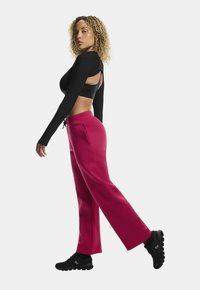 Zwarte langemouwtop met een uitsparing op de rug, gecombineerd met losse, hooggeplaatste roze sweatpants en zwarte gestructureerde sportschoenen.