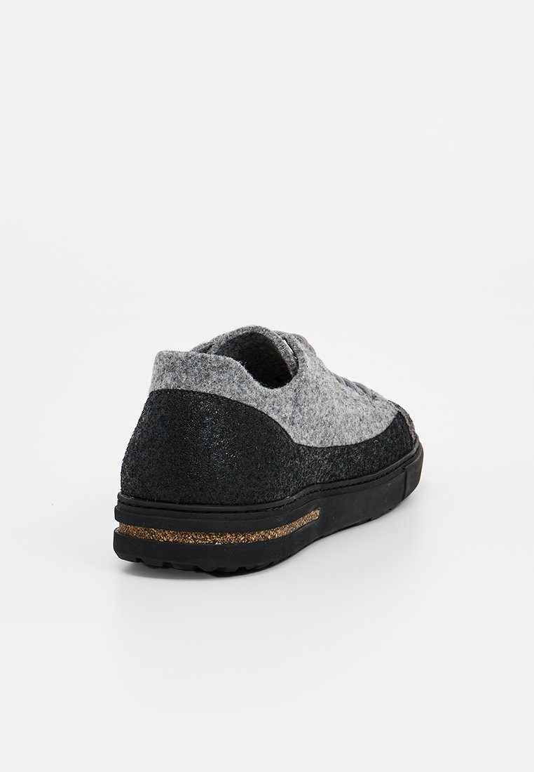 Zapato slip-on en gris y negro con parte superior de fieltro texturizado, suela de goma y franja de acento dorado. Forma redondeada y diseño de perfil bajo.