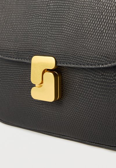 Τσάντα χειρός από μαύρο δερματίνη με ανάγλυφη υφή, που διαθέτει χρυσή γεωμετρική αγκράφα. Επίπεδο, δομημένο σχέδιο με ακριβείς ραφές.