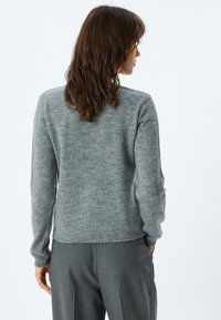 Maglione grigio a maglia con maniche lunghe, scollo rotondo e orlo a coste. Realizzato in materiale morbido, presenta una finitura leggermente strutturata.